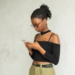 A young African American woman using a smartphone indoors, focusing on the screen.